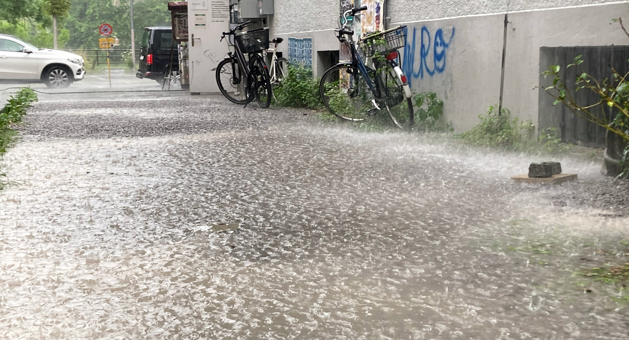 Una strada allagata sotto la pioggia battente con biciclette appoggiate a un edificio.