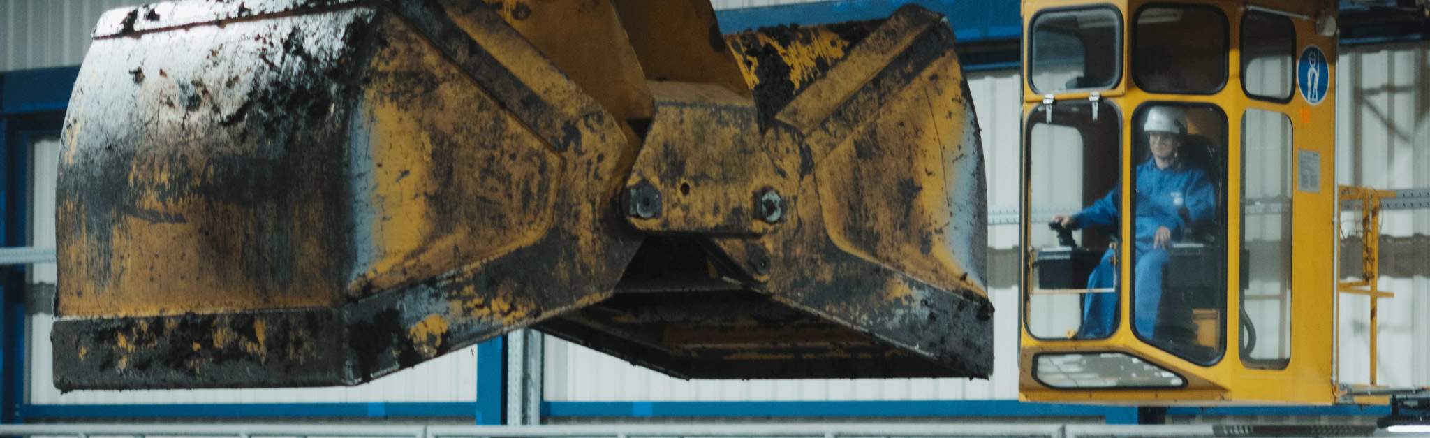 Ein Bauarbeiter bedient einen großen orangefarbenen Bagger in einer Industrieanlage.